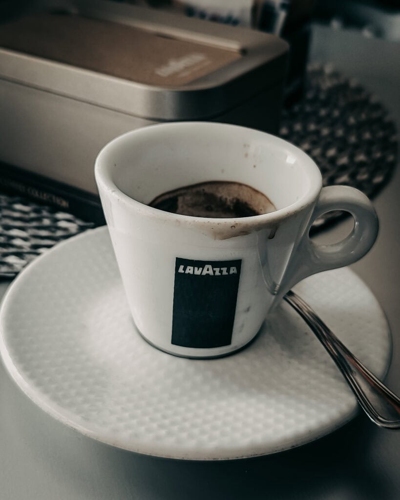 A cup of hot coffee in a Lavazza branded mug on a white saucer.