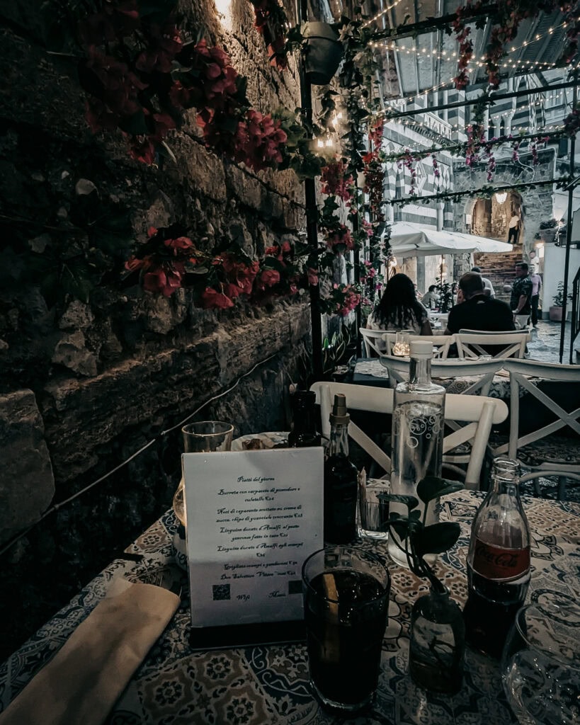 Outdoor dining area with flowers, string lights, and table settings.