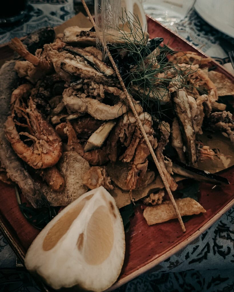 Assorted fried seafood with lemon wedge and herbs on a wooden platter.