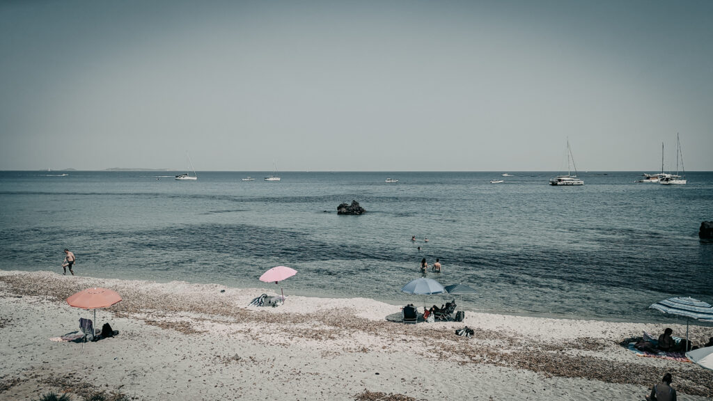 People relaxing on the beach with umbrellas and boats in the water.
