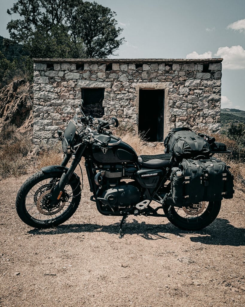 Black adventure motorcycle with luggage parked in front of a stone building.