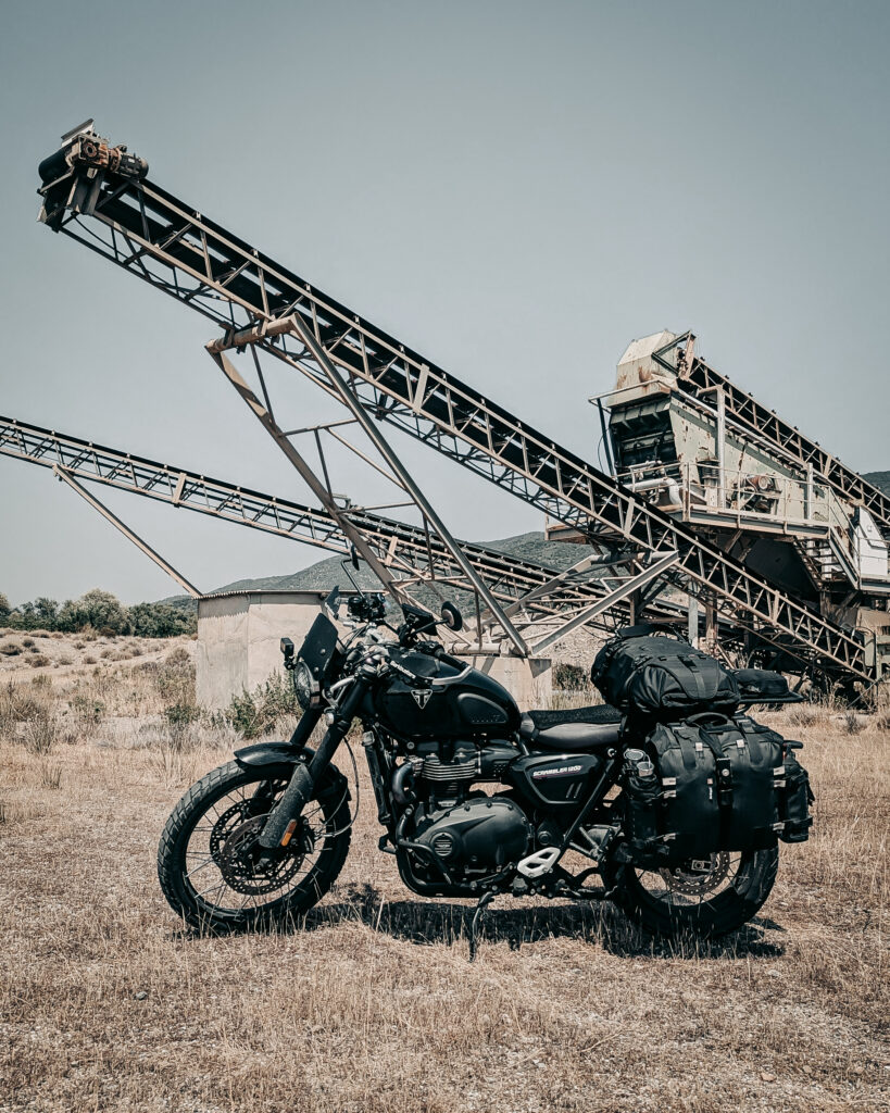 Black scrambler motorcycle with luggage in front of conveyor belt system.