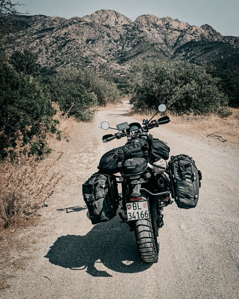 Motorcycle with panniers on dirt trail in mountainous landscape.