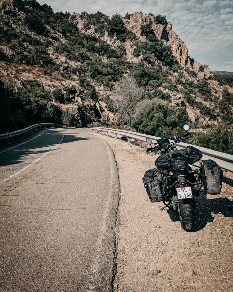 Motorcycle parked on mountain road with scenic rocky landscape.