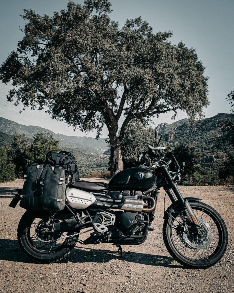 Black scrambler motorcycle with luggage in scenic outdoor setting.