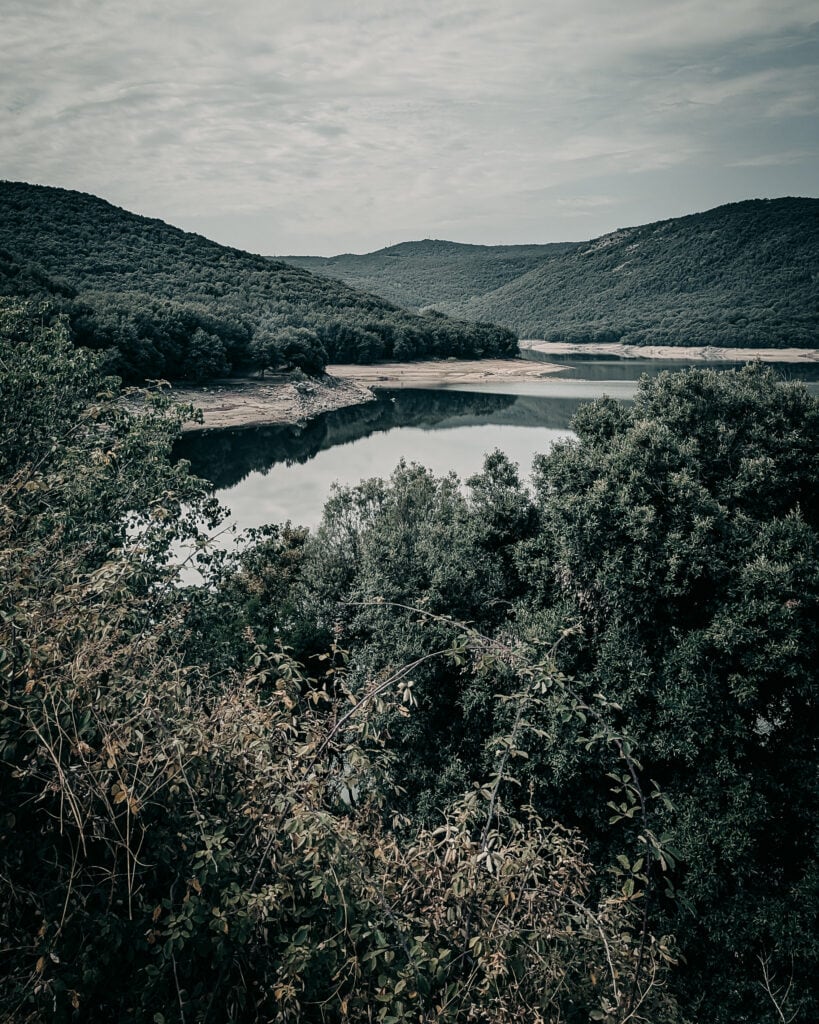 Serene river flowing through green hills under cloudy sky.
