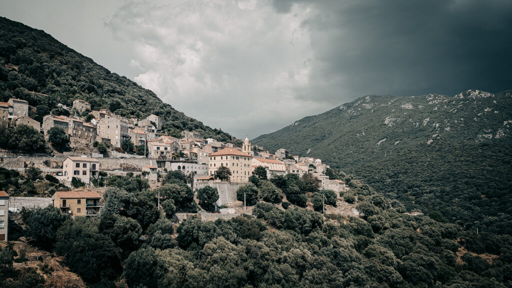 Picturesque hillside village with lush greenery and mountain backdrop in Italy.