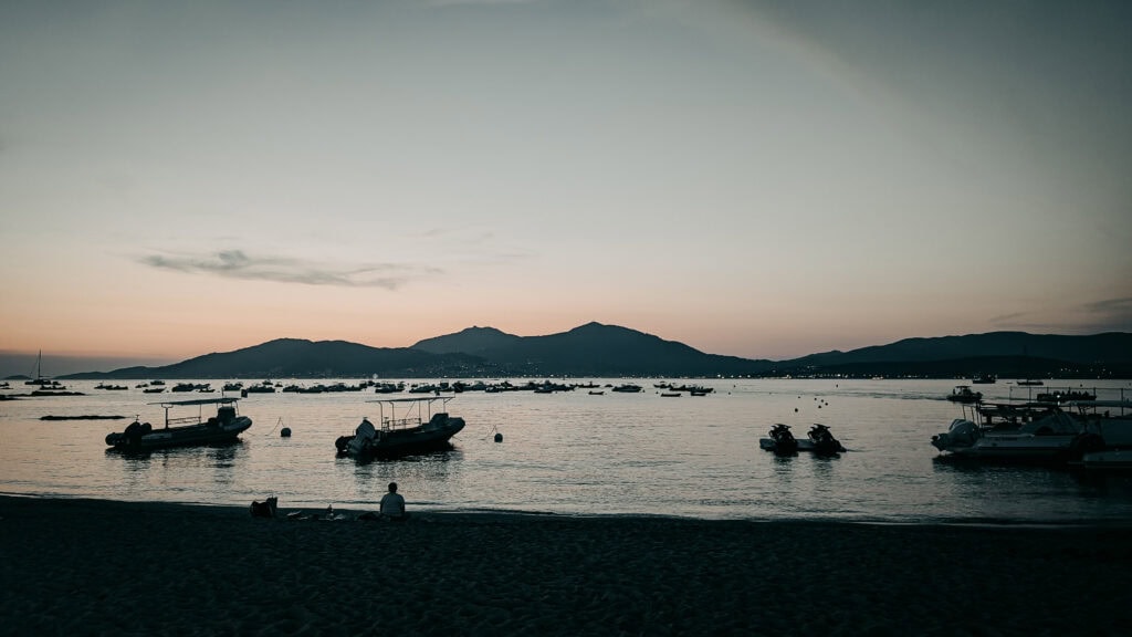 Calm lake with boats at sunset and mountain backdrop.