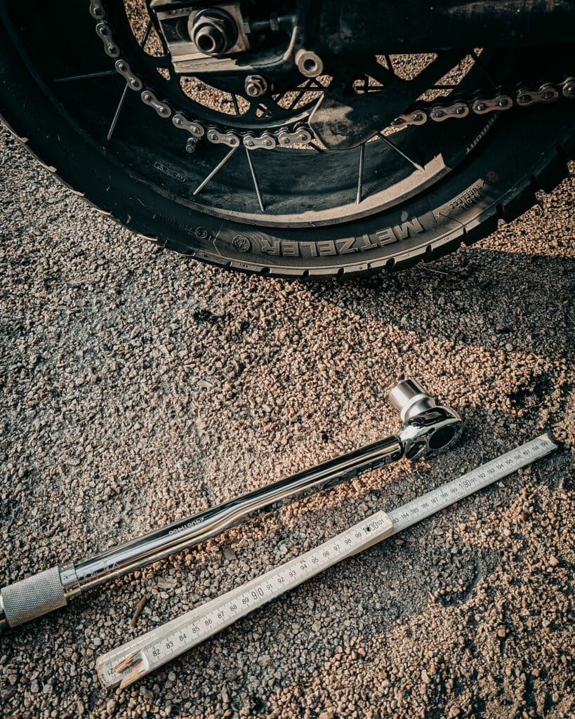 Close-up of motorcycle wheel with a torque wrench and ruler on asphalt.