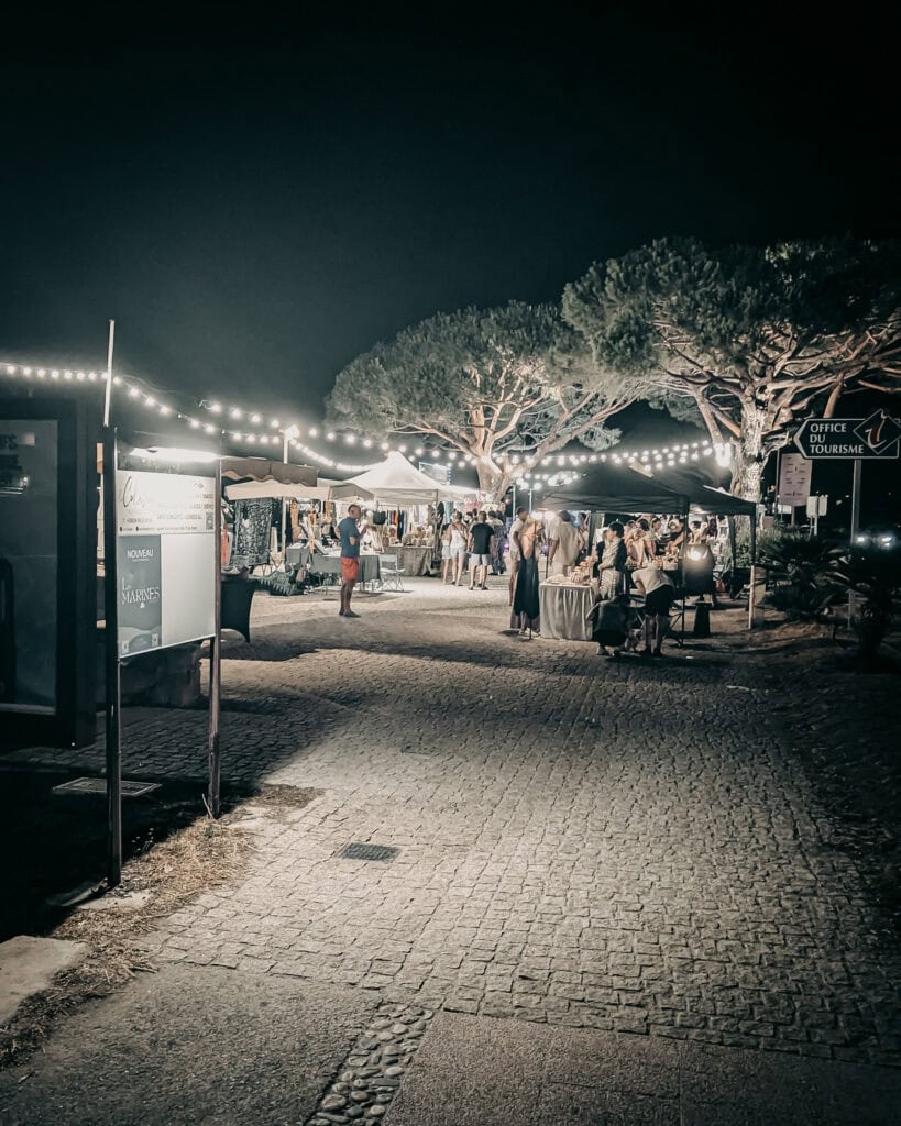Night market with string lights, vendors, and visitors at outdoor event.