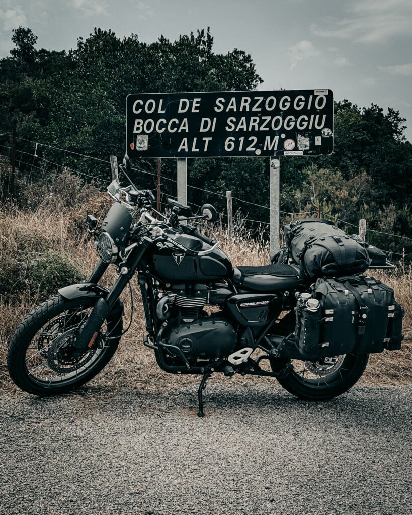 Black motorcycle with luggage near Col de Sarzoggio sign.