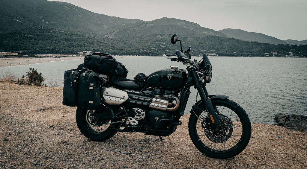 Adventure motorcycle with gear parked by lake with mountains in background.