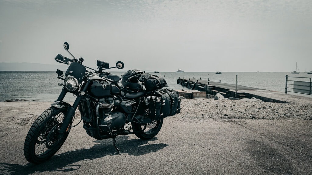 Classic black motorcycle parked near the beach with calm sea in background.