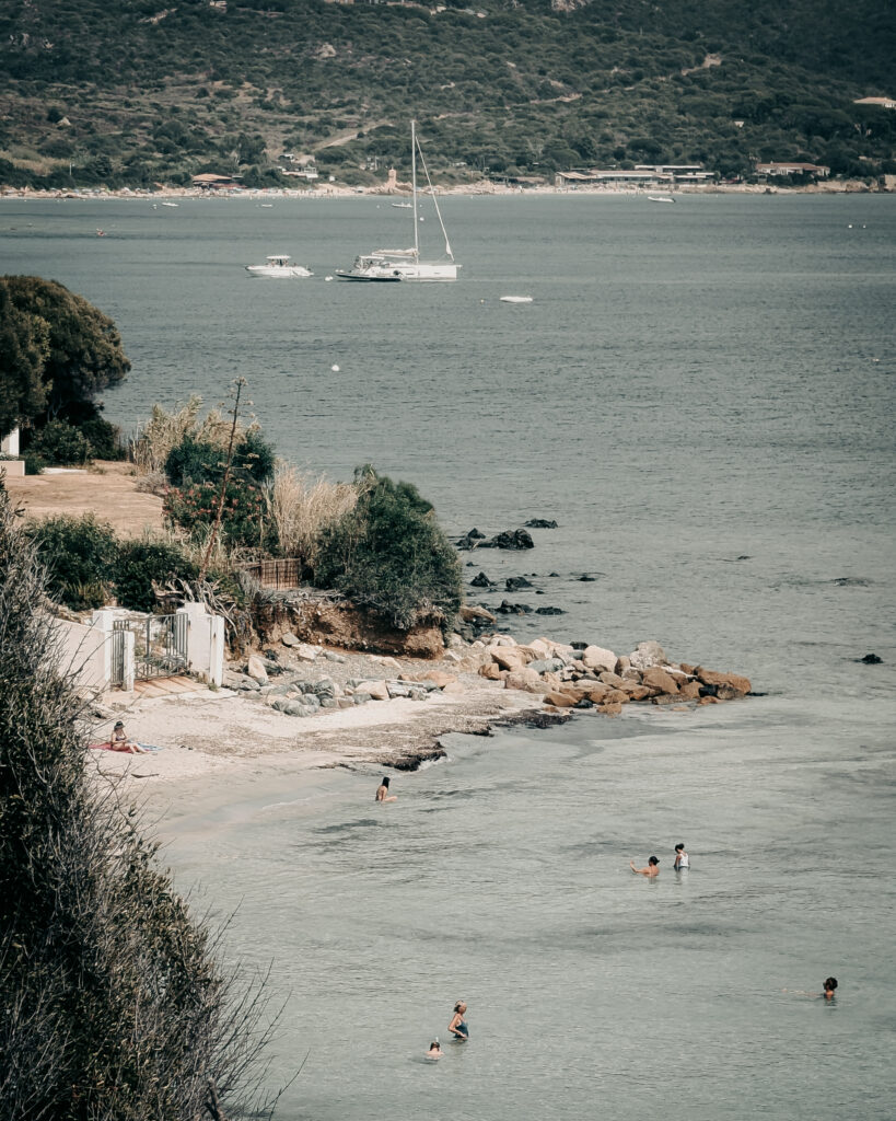 Beautiful coastal scene with sailboats, beach, and swimmers in the water.