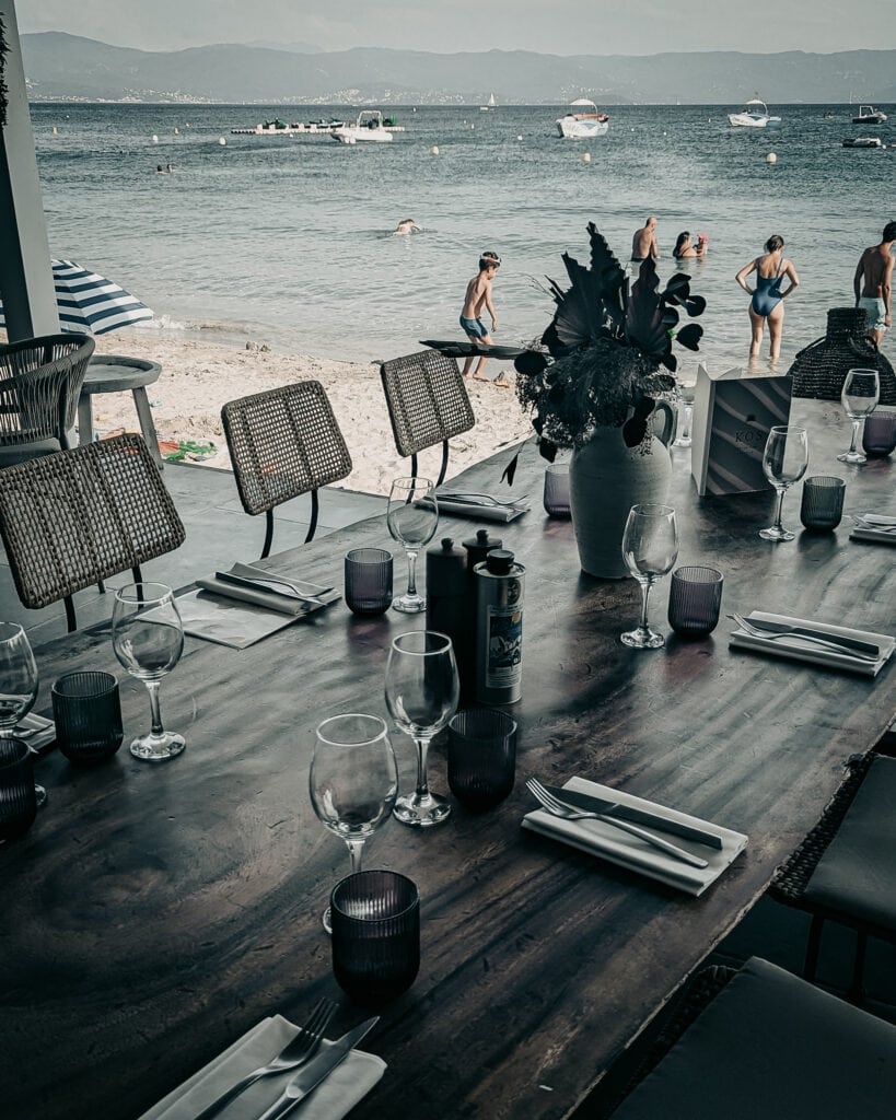 Beachside restaurant with ocean view, tables set for dining, and people enjoying the beach.