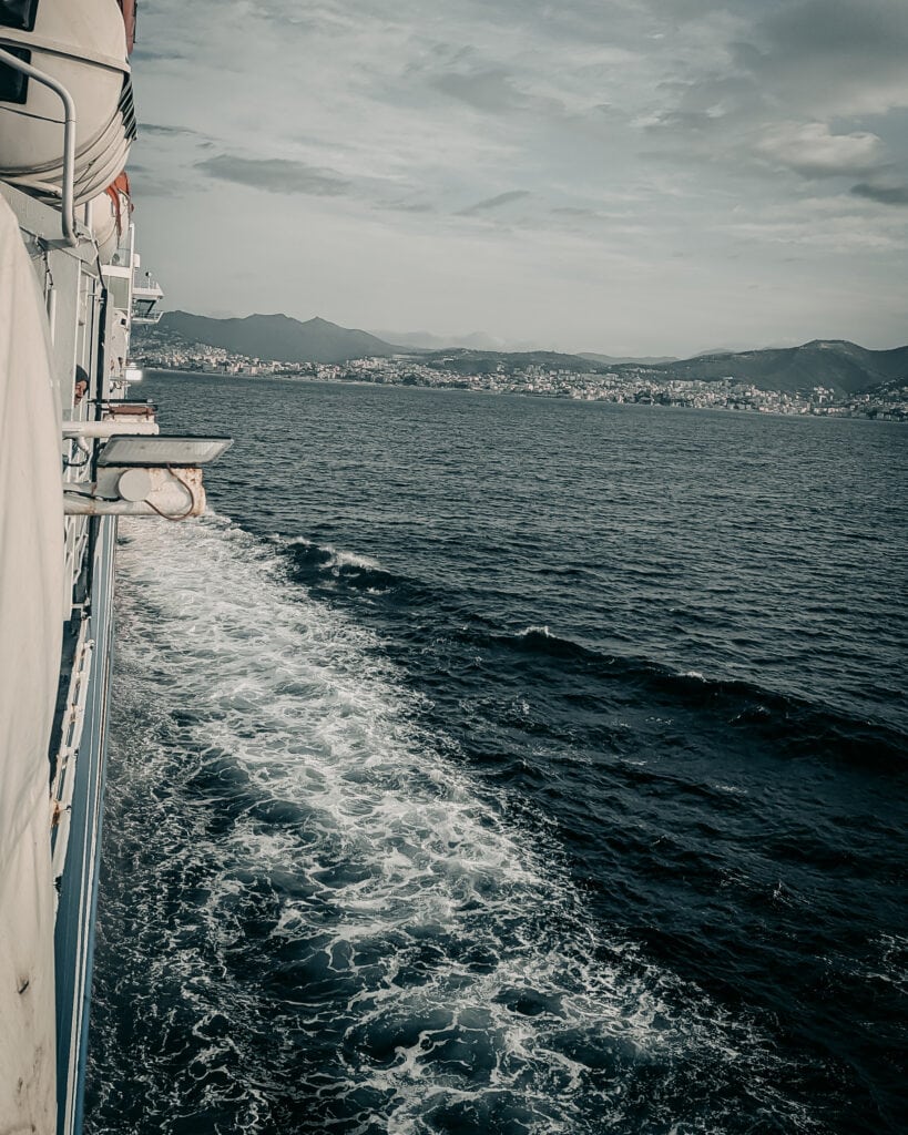 View from a boat showing water, distant shoreline, and mountains under cloudy sky.